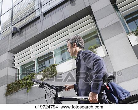 Picture - Business man carrying bicycle outdoors low angle view side view. Fotosearch