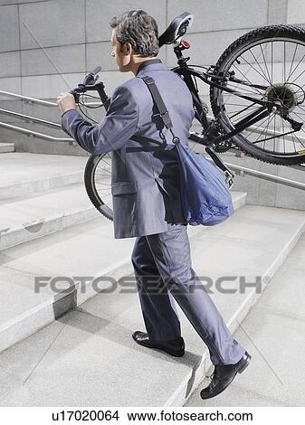 Business man carrying bicycle up steps side view View Large Photo Image Picture - Business man carrying bicycle up steps side view. Fotosearch