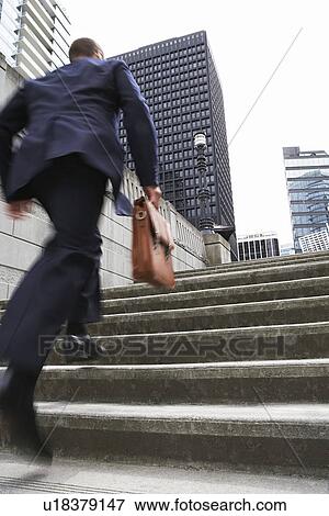 Business man carrying briefcase ascending steps low angle view View Large Photo Image Stock Photo - Business man carrying briefcase ascending steps low angle view. Fotosearch