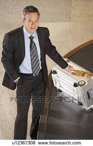 Business man claiming suitcase at luggage carousel in airport View Large Photo Image Stock Photo - Business man claiming suitcase at luggage carousel in airport. Fotosearch