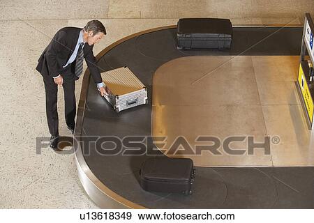Business man claiming suitcase at luggage carousel in airport View Large Photo Image Stock Photo - Business man claiming suitcase at luggage carousel in airport. Fotosearch