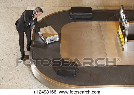 Business man claiming suitcase at luggage carousel in airport View Large Photo Image Stock Photograph - Business man claiming suitcase at luggage carousel in airport. Fotosearch