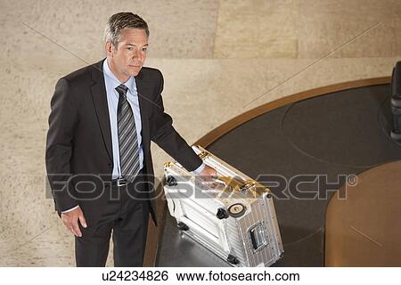 Stock Photograph - Business man claiming suitcase at luggage carousel in airport. Fotosearch