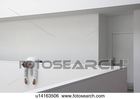 Stock Photograph - Business man hanging over hallway balustrade. Fotosearch