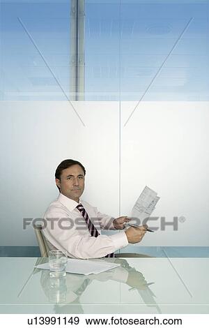 Business man holding document at table in conference room portrait View Large Photo Image Stock Photo - Business man holding document at table in conference room portrait. Fotosearch
