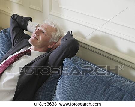 Stock Image - Business man leaning back on sofa elevated view. Fotosearch