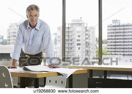 Business man leaning on desk in office View Large Photo Image Stock Image - Business man leaning on desk in office. Fotosearch