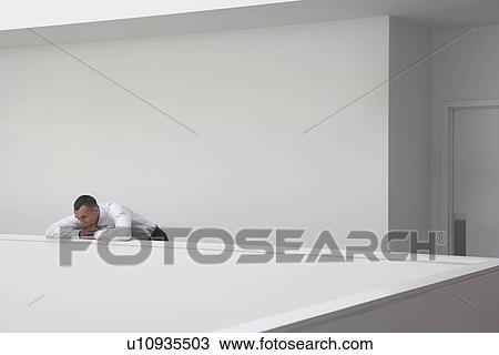 Stock Image - Business man leaning on hallway balustrade. Fotosearch