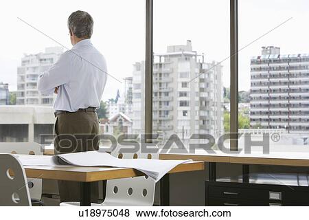 Stock Photo - Business man looking out of office window back view. Fotosearch