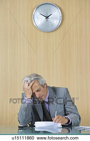 Stock Image - Business man reading papers in office with head in hands. Fotosearch