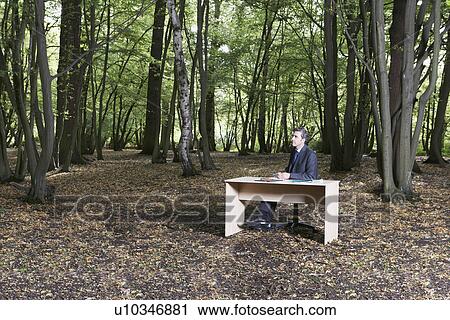Business man sitting at desk in middle of forest thinking View Large Photo Image Stock Image - Business man sitting at desk in middle of forest thinking. Fotosearch