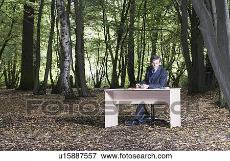 Business man sitting at desk in middle of forest working View Large Photo Image Stock Photo - Business man sitting at desk in middle of forest working. Fotosearch