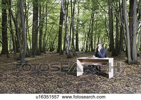 Business man sitting at desk in middle of forest View Large Photo Image Stock Photo - Business man sitting at desk in middle of forest. Fotosearch
