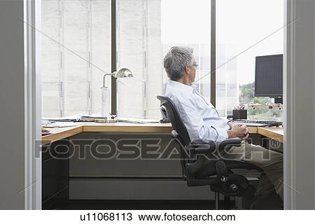 Business man sitting at desk in office side view View Large Photo Image Stock Image - Business man sitting at desk in office side view. Fotosearch