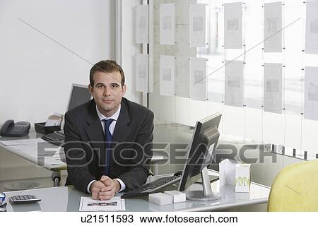 Stock Image - Business man sitting at desk in office portrait. Fotosearch