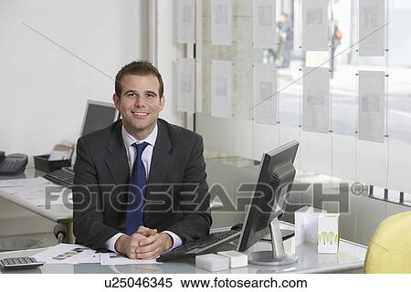 Stock Photography - Business man sitting at desk in office portrait. Fotosearch