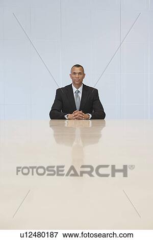 Stock Photo - Business man sitting at end of conference table portrait. Fotosearch