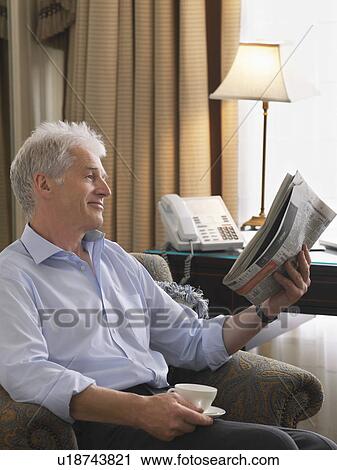 Stock Image - Business man sitting in armchair reading newspaper. Fotosearch