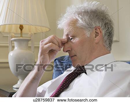 Stock Photo - Business man sitting on sofa pinching bridge of nose close-up side view. Fotosearch