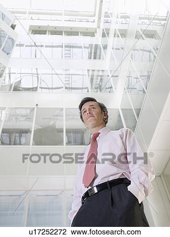Business man standing in atrium of office building low angle view View Large Photo Image Stock Image - Business man standing in atrium of office building low angle view. Fotosearch