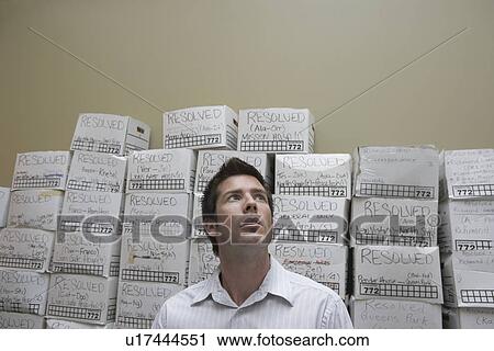 Stock Image - Business man standing in front of stack of filing boxes in storage room low angle view. Fotosearch