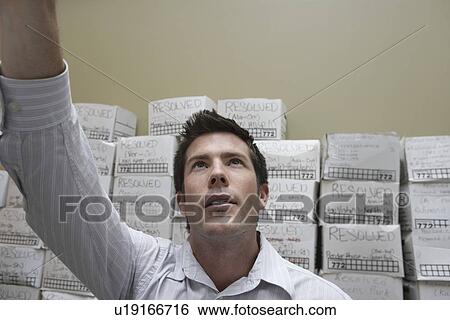 Business man standing in front of stack of filing boxes in storage room reaching up low angle view View Large Photo Image Stock Photograph - Business man standing in front of stack of filing boxes in storage room reaching up low angle view. Fotosearch