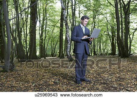 Business man standing in middle of forest typing on laptop View Large Photo Image Stock Image - Business man standing in middle of forest typing on laptop. Fotosearch