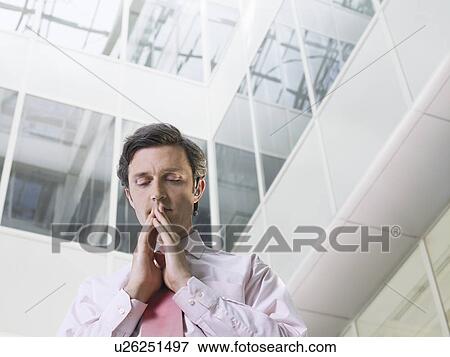 Business man standing with clasped hands in atrium of office building low angle view View Large Photo Image Stock Photo - Business man standing with clasped hands in atrium of office building low angle view. Fotosearch