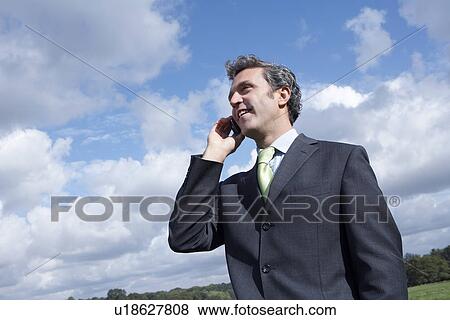 Stock Photo - Business man talking on mobile phone in meadow. Fotosearch
