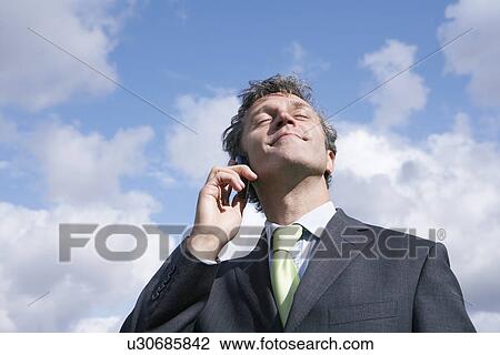 Business man talking on mobile phone smiling sky in background View Large Photo Image Stock Image - Business man talking on mobile phone smiling sky in background. Fotosearch