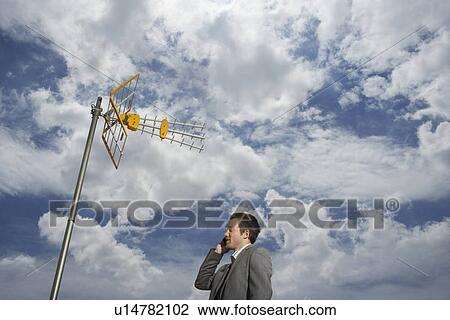 Business man using cell phone underneath satellite tower View Large Photo Image Stock Image - Business man using cell phone underneath satellite tower. Fotosearch