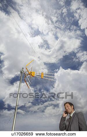 Stock Photo - Business man using cell phone underneath satellite tower. Fotosearch