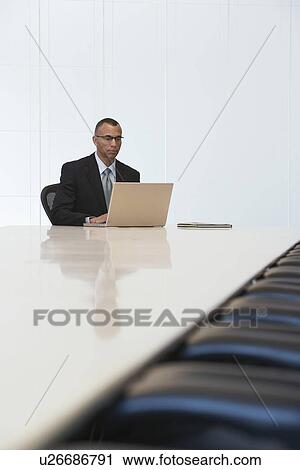 Stock Image - Business man using laptop in board room. Fotosearch