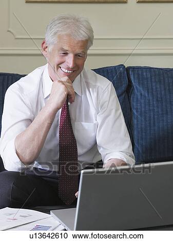 Stock Image - Business man using laptop sitting on sofa. Fotosearch