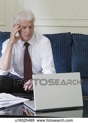 Stock Photo - Business man using laptop sitting on sofa. Fotosearch