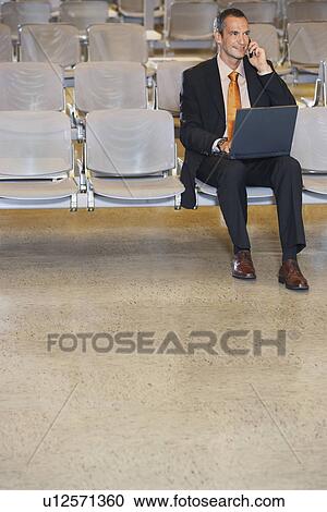 Business man using mobile phone and laptop in airport lobby View Large Photo Image Stock Image - Business man using mobile phone and laptop in airport lobby. Fotosearch