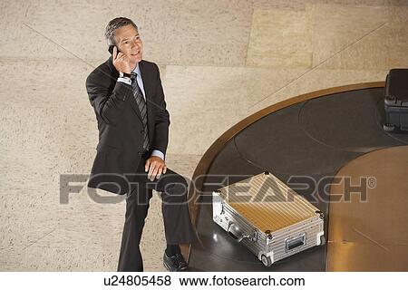 Stock Photo - Business man using mobile phone at luggage carousel in airport. Fotosearch