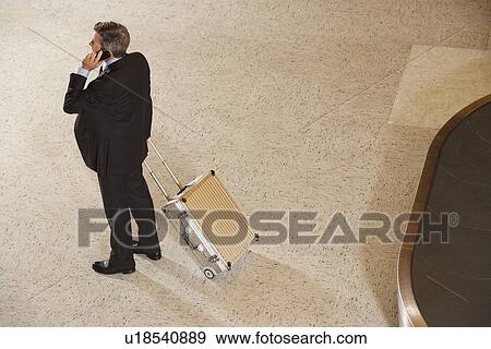 Stock Photo - Business man using mobile phone by baggage claim in airport. Fotosearch