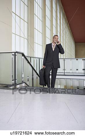Business man using mobile phone in airport lobby on stairs View Large Photo Image Picture - Business man using mobile phone in airport lobby on stairs. Fotosearch