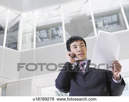Stock Photo - Business man using mobile phone in atrium of office building low angle view. Fotosearch