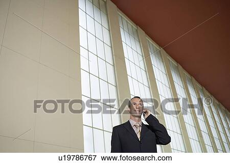 Business man using mobile phone in airport lobby View Large Photo Image Stock Photo - Business man using mobile phone in airport lobby. Fotosearch
