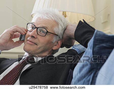 Business man using mobile phone sitting on sofa close-up View Large Photo Image Stock Photo - Business man using mobile phone sitting on sofa close-up. Fotosearch