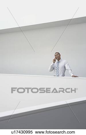 Stock Photography - Business man using mobile phone standing by hallway balustrade. Fotosearch