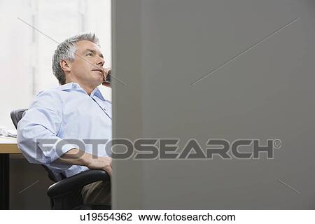 Stock Image - Business man using phone in office through door. Fotosearch