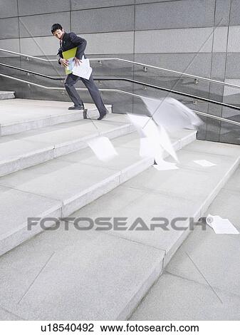 Stock Image - Business man walking up steps losing papers from briefcase outdoors side view. Fotosearch