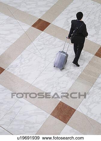 Stock Photo - Business man walking with suitcase elevated view back view. Fotosearch