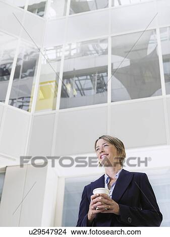 Picture - Business woman holding cup of coffee standing in atrium of office building low angle view. Fotosearch
