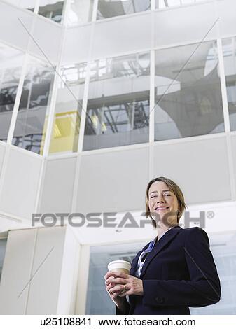 Business woman holding cup of coffee standing in atrium of office building low angle view View Large Photo Image Stock Image - Business woman holding cup of coffee standing in atrium of office building low angle view. Fotosearch