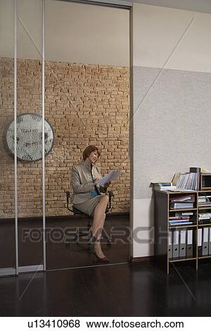 Stock Photo - Business woman reading paper sitting in office doorway. Fotosearch