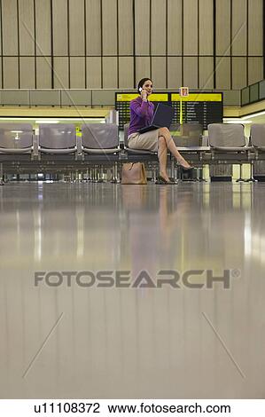 Stock Image - Business woman using mobile phone in airport lobby. Fotosearch